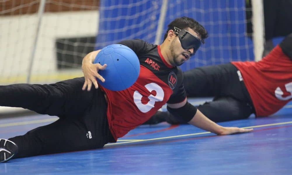 Mas - Regional Nordeste de Goalball. O pivô Renan, da Apace, joga o corpo para o lado esquerdo e se apoia sobre o braço para defender, enquanto abraça a bola com a mão direita