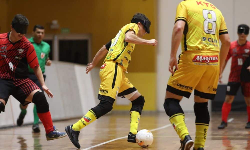 Ricardinho passa pela marcação de Alefe e conduz a bola com o pé esquerdo. Jogador, que é branco, magro e tem o cabelo castanho, veste uniforme amarelo da Agafuc (Renan Cacioli/CBDV)