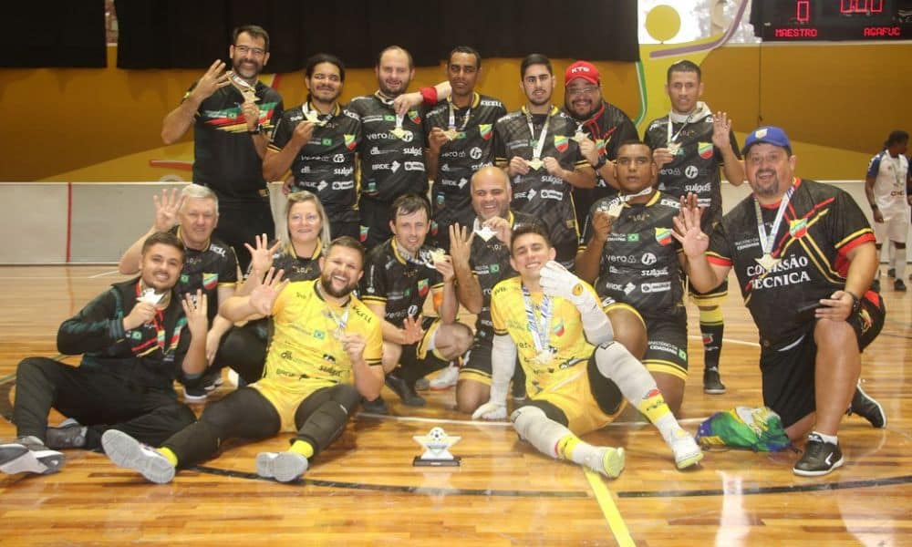 Equipe da Agafuc posa para foto. Os atletas têm medalhas de ouro no pescoço, enquanto a taça está no chão ao centro