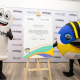 Personagem de preservativo e Piu, mascote de Santiago 2023, pousam para foto em frente ao contrato de assinatura de parceria entre Lifestyle e comitê organizador