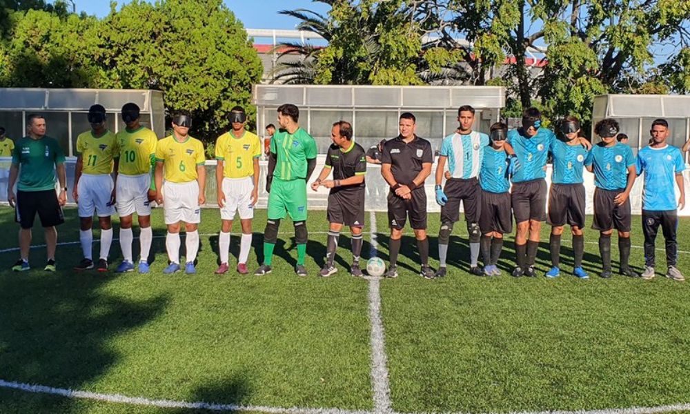 Equipes juvenis de Brasil, à esquerda, e Argentina, à direita da imagem, estão perfiladas no centro do gramado ao lado da arbitragem antes do jogo pela Copa Tango de futebol de cegos (Foto: Fadec/Divulgação)