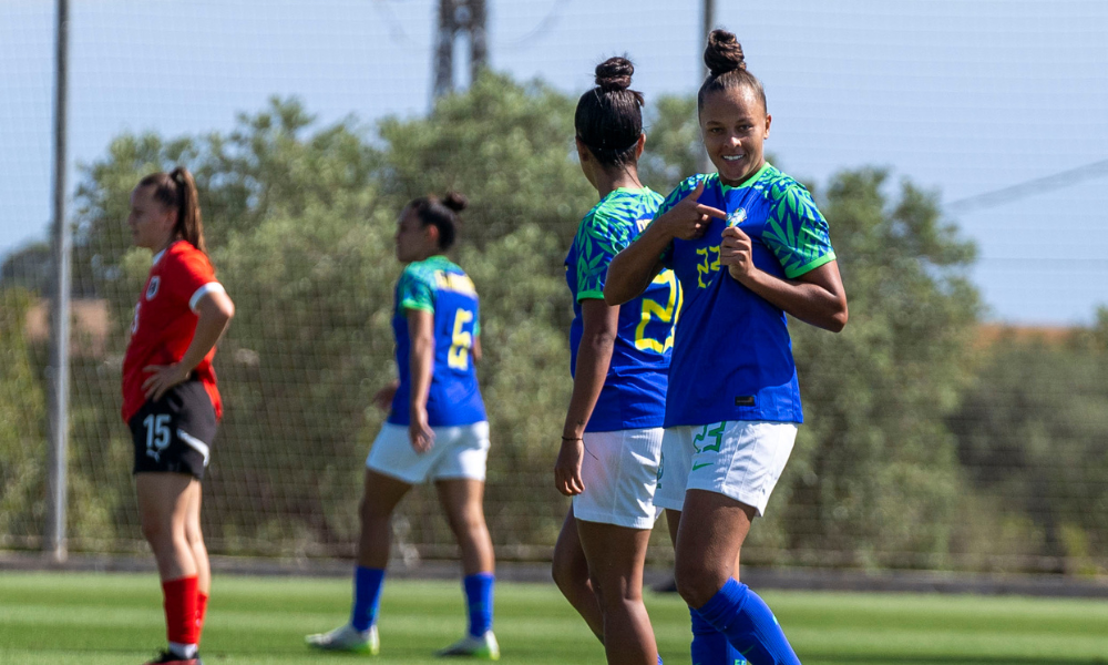 Milena aponta para o escudo da CBF, com a camisa azul, e comemora vitória do Brasil sobre a Áustria em amistoso de futebol feminino sub-20