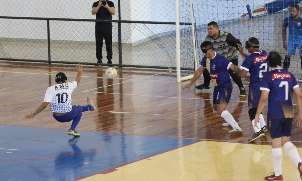 Maxwell chuta com a perna esquerda enquanto equilibra o corpo na perna direita, dobrada quase 90 graus e os braços erguidos cada um para um lado; à frente dele o goleiro do Ismac aguarda, e outros atletas de sua equipe aparecem à direita. Foto: Renan Cacioli/ CBDV.