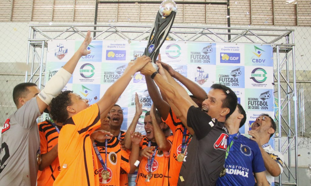 Equipe da Acelgo ergue o troféu do Regional Centro-Norte com vários atletas tocando na taça, sustentada principalmente nas mãos do técnico Fabrício Gomes. Fotos: Renan Cacioli/ CBDV.