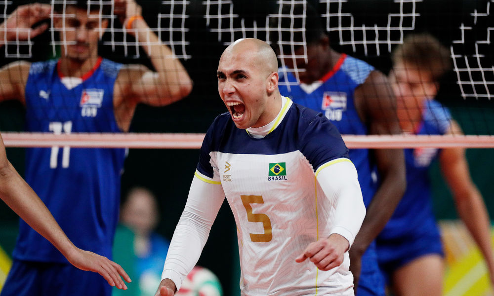 Matheus Brasília vibra com a camisa branca da seleção brasileira de vôlei masculino com jogadores de Cuba ao fundo. Ele foi convocado para enfrentar o Irã na Liga das Nações, a VNL