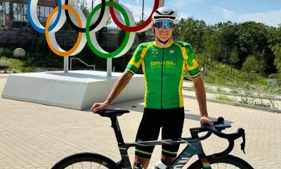 Na imagem, Vinícius Rangel com sua bicicleta e os anéis olímpicos ao fundo Movistar